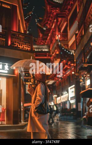 Donna che si allontana sotto un ombrello in un affollato mercato notturno, Giardino Yuyuan, Shanghai, Cina Foto Stock
