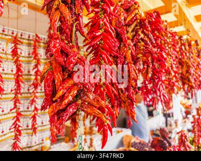 Mazzi di peperoncini rossi brillanti appesi ad asciugare a una bancarella tradizionale di mercato locale a Funchal, Madera, Portogallo. Foto Stock