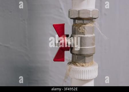 Valvola a sfera in metallo con maniglia a farfalla rossa installata su tubo di plastica bianco per idraulica all'interno Foto Stock