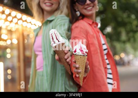 Amici felici che mostrano coni di waffle con deliziosa gelata nel parco, messa a fuoco selettiva Foto Stock