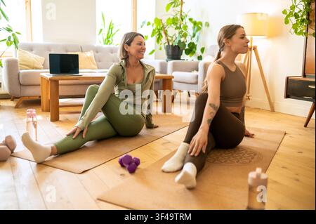 Giovane allenatore felice e donna matura che eseguono uno stretching seduto della colonna vertebrale Foto Stock