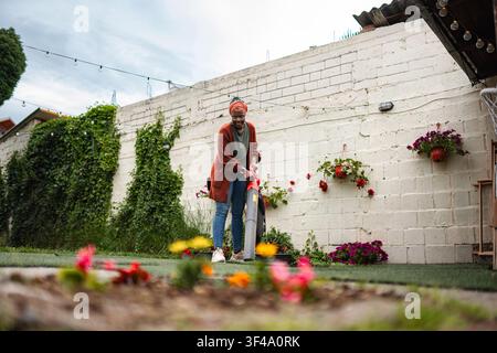 Donna sorridente che usa un soffiatore per foglie durante i lavori in giardino Foto Stock
