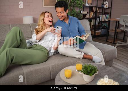 Coppia che si rilassa sul divano a casa ridendo con lo smartphone Foto Stock