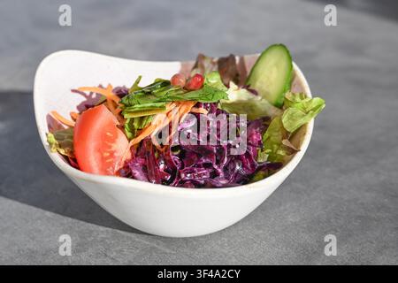 Insalata estiva fresca con una leggera condimento in una ciotola, preparata con verdure come cavolo rosso, carote, lattuga, cetrioli e pomodori, spazio libero, sele Foto Stock