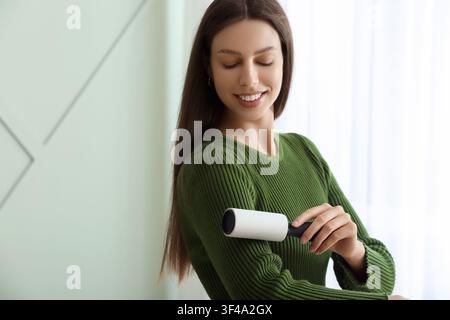 Giovane donna che usa un rullo anti pelucchi sul suo maglione verde, concetto di pulizia e cura dei capi di abbigliamento, faccende domestiche e manutenzione della casa Foto Stock