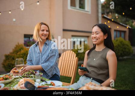 Amiche donne multi etniche che godono di una cena all'aperto nel cortile Foto Stock