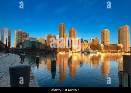 Luce dorata del mattino all'alba sulla città di Boston con riflessi sull'acqua calma del porto Foto Stock