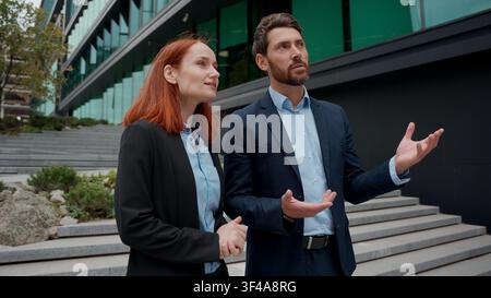 Due partner commerciali caucasici, donna e uomo, si incontrano in città, si stringono la mano e discutono di uomini d'affari edificio per uffici imprenditori uomo d'affari adulto Foto Stock