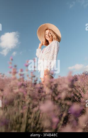 Donna lavanda estate felice giovane donna in abito bianco e cappello di paglia in piedi in un campo fiorito sotto un cielo blu soleggiato Foto Stock
