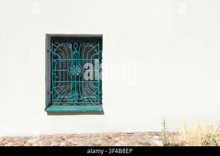 Sfondo di sbarre di finestra vintage in ferro battuto verde. Grata di sicurezza decorata e ornata su un edificio classico della vecchia città con muro in stucco bianco e spazio libero Foto Stock