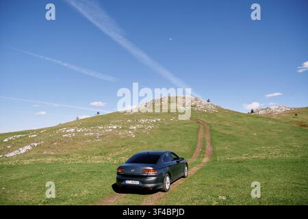 L'auto procede lungo una strada di campagna su una pianura verde in salita. Vista posteriore. Foto Stock