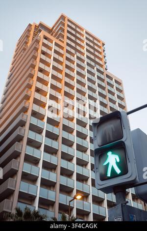 Prospettiva a basso angolo che guarda verso l'alto di un alto grattacielo residenziale moderno dietro un semaforo pedonale al tramonto, Osaka, Giappone Foto Stock