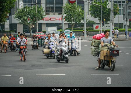 Shanghai, Cina - 5 agosto 2017: Una strada larga è piena di persone in bicicletta, biciclette elettriche e scooter; un uomo su una bicicletta elettrica Foto Stock