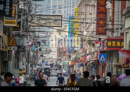Shanghai, Cina – 06 agosto 2017: Una strada stretta a Shanghai è densamente popolata da cavi elettrici sospesi, numerose vetrine di negozi e una folla di Foto Stock