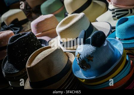 Un primo piano mostra una esposizione fittamente imbottita di cappelli di paglia e tessuto assortiti, tra cui fedora, cappelli da sole e un cappello per bambini azzurro con bl Foto Stock