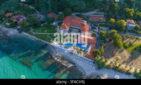 Afytos, Grecia, 15 luglio 2025. Ripresa aerea dell’Afitis Boutique Hotel con edifici dai tetti rossi, piscine, sdraio e un mare blu cristallino Foto Stock