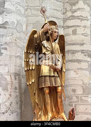 Statua dorata di San Michele che sconfigge un drago all'interno di una cattedrale. Antica statua dorata dell'arcangelo Michele che abbatte un drago in una st storica Foto Stock