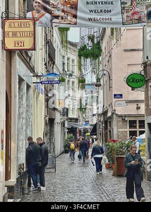 Stretta strada storica a Bruxelles con vecchi cartelli di ristoranti e pedoni. Affascinante vicolo lastricato a Bruxelles con restaura tradizionale Foto Stock
