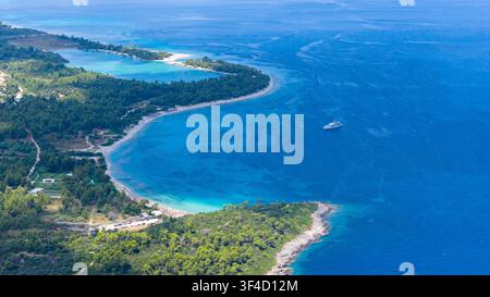 Vista aerea alta di insenature di sabbia curve, acqua blu limpida e fitta foresta costiera, con una piccola barca al largo a Golden Beach, Grecia. Foto Stock