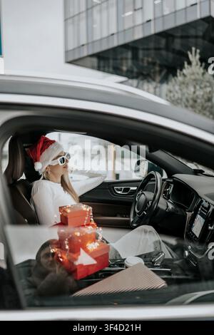 Donna con cappello di Babbo Natale seduta in un'auto circondata da regali durante la stagione festiva Foto Stock