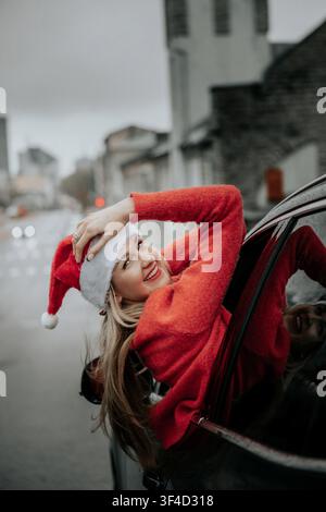 Donna indossa un cappello di Babbo Natale mentre si gode una corsa festosa nella strada della città in una giornata nuvolosa Foto Stock