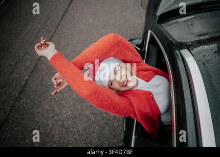 Donna in maglione rosso e cappello di Natale si sporge dal finestrino dell'auto durante l'inverno Foto Stock