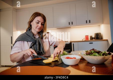 Donna prepara verdure e frutta in cucina per un pasto sano a casa durante il giorno Foto Stock