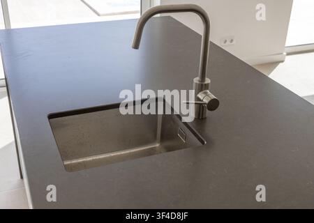 Una vista ravvicinata di un'isola da cucina in pietra grigio scuro con un lavello sottotop senza giunzioni e un rubinetto contemporaneo in nichel spazzolato Foto Stock