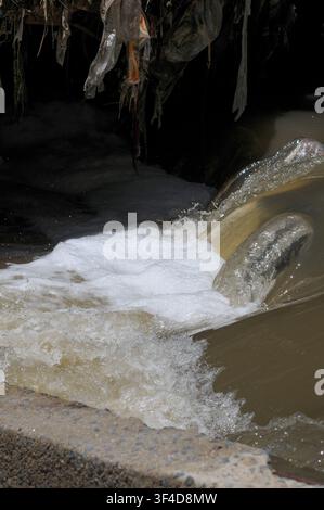 Acqua schiumosa inquinata e detriti di plastica che fluiscono da uno scarico pluviale nel fiume Hennops nel Gauteng, Sudafrica, illustrando il deflusso urbano, wa Foto Stock