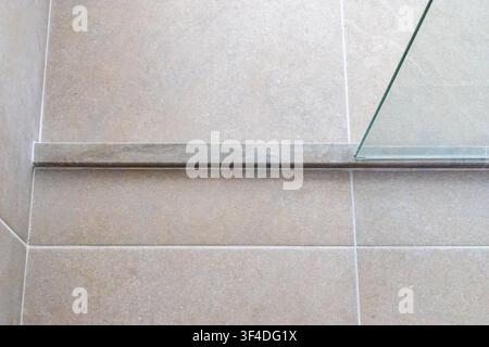 Una vista ravvicinata della base di una cabina doccia contemporanea, con pavimento piastrellato beige e una partizione in vetro trasparente Foto Stock