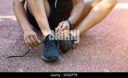 Millennial runner che legano i pattini mentre si siede sulla strada durante il suo addestramento, primo piano Foto Stock