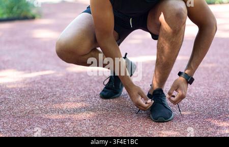 Vista closeup di jogger nero che legano i lacci sulle sue scarpe sportive durante il suo allenamento all'esterno Foto Stock