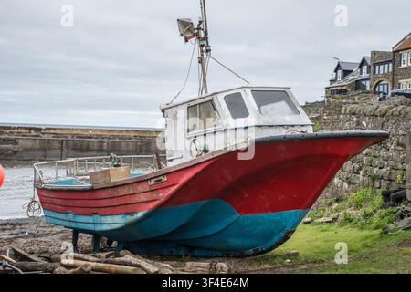 Un piccolo vecchio peschereccio tirato fuori dall'acqua, Craster Harbour, Northumberland, Inghilterra Foto Stock