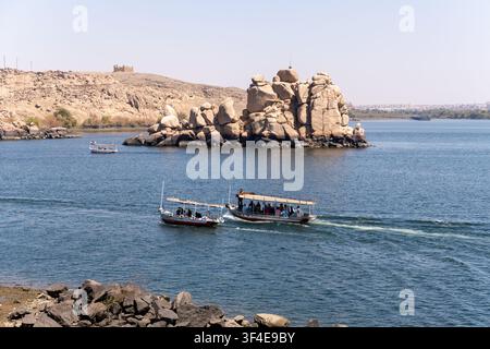 Tempio di Philae, Egitto - 10 marzo 2026: Turisti che si godono una gita in barca lungo il Nilo, passando accanto a isole rocciose e il paesaggio desertico dell'Egitto Foto Stock