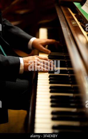 Primo piano delle mani di un uomo in abito scuro e polsini bianchi che suona i tasti di un pianoforte a coda antico. Foto Stock