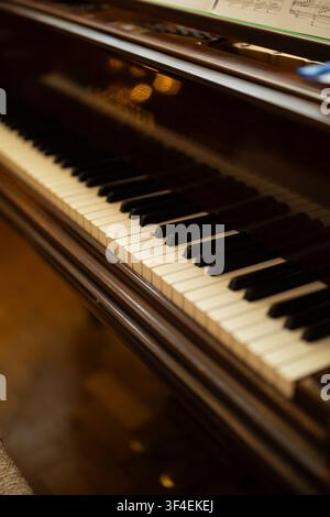 Dettaglio ravvicinato dei tasti bianchi e neri di un pianoforte a coda antico, con uno spartito visibile sullo sfondo. Foto Stock