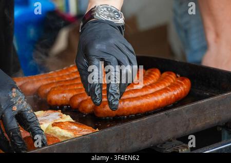 Prima piano di un uomo che cucina salsicce su un barbecue. Street food. Salsicce. Fast food Foto Stock