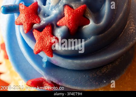 Ghirlande di glassa blu con decorazioni a stella rosse. Caramelle a forma di stella poggiate su una glassa cremosa. Accenti rosso acceso contrastano con la base blu fredda. Primo piano- Foto Stock