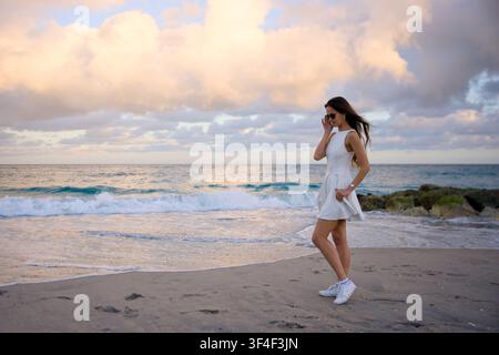 Donna in vestito bianco in piedi su una larga spiaggia sabbiosa Foto Stock
