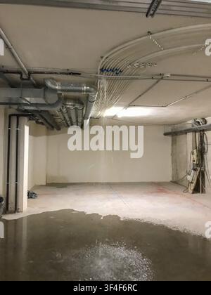 Costruzione di edifici che presentano perdite d'acqua dai tubi esposti sul pavimento di cemento, creando una grande pozzanghera e potenziali danni in un locale vuoto, Foto Stock
