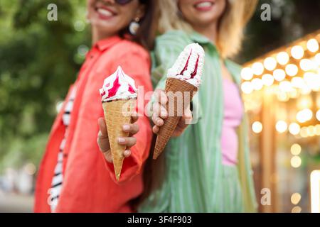 Amici felici che mostrano coni di waffle con deliziosa gelata nel parco, messa a fuoco selettiva Foto Stock