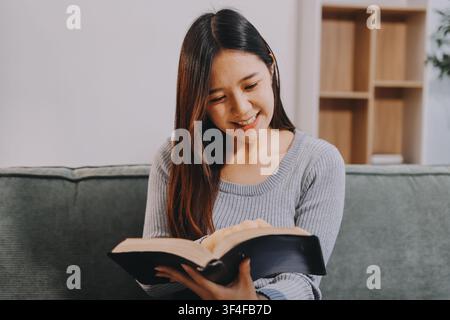 Giovane donna leggendo un libro sul divano di casa Foto Stock