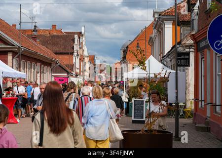 Kuldiga, Lettonia - 25 luglio 2026: Folle passeggiano attraverso un vivace festival della Vecchia Città con bancarelle di mercato, negozi e architettura storica in una giornata estiva Foto Stock