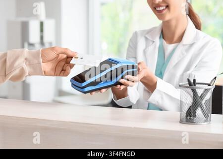 Mano maschile con carta di credito che paga tramite terminale alla reception in clinica Foto Stock