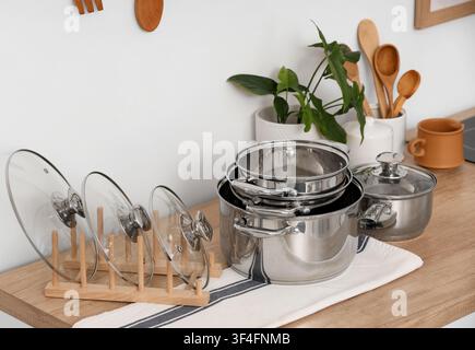 Pentole e padelle in acciaio inossidabile con coperchi in vetro su un piano di lavoro in legno in un contesto di cucina moderna, il set di utensili da cucina include varie dimensioni, con alcuni p Foto Stock