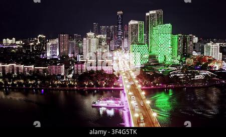 LIUZHOU, CINA – 10 GIUGNO 2024: Una vista aerea del traffico che attraversa un ponte luminoso verso grattacieli verdi illuminati di notte a Liuzhou, Chin Foto Stock