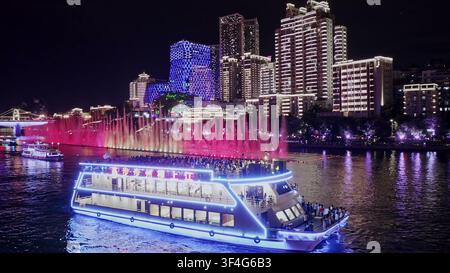 LIUZHOU, CINA – 10 GIUGNO 2024: Un battello turistico illuminato scende il fiume passando davanti a fontane d'acqua rosa e grattacieli illuminati di notte a Liuzhou, in Cina Foto Stock