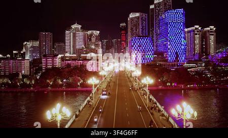 LIUZHOU, CINA - 10 GIUGNO 2024: Una prospettiva aerea simmetrica lungo un ponte luminosamente illuminato che conduce verso grattacieli viola illuminati di notte Foto Stock