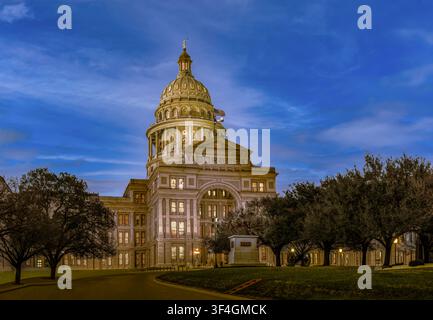 Capitolo dello Stato del Texas illuminato al crepuscolo ad Austin, con la sua cupola e la facciata storica incorniciata da alberi sotto un drammatico cielo blu serale. Foto Stock