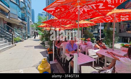 TORONTO, CANADA - 15 LUGLIO 2024: I clienti godono di bevande e pranzo su una terrazza all'aperto sotto ombrelloni rossi a Yorkville, Toronto, Canada. Foto Stock